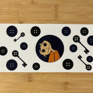 May include: A white sticker sheet with a black and white illustration of a girl with a button nose and a keyhole mouth. The sticker sheet also includes black buttons and keys.