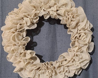 May include: A beige burlap wreath with a ruffled design. The wreath is made of a natural material and has a rustic look.
