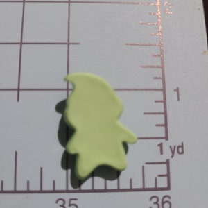 May include: A light green, flat, plastic gnome figurine. The gnome is wearing a pointed hat and has a beard.