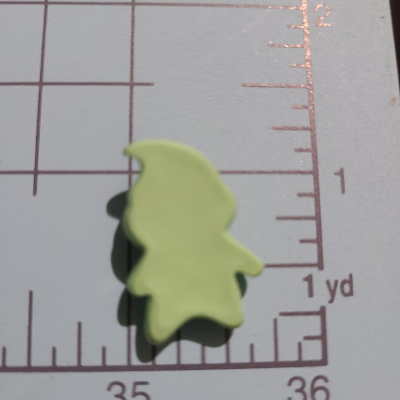 May include: A light green, flat, plastic gnome figurine. The gnome is wearing a pointed hat and has a beard.
