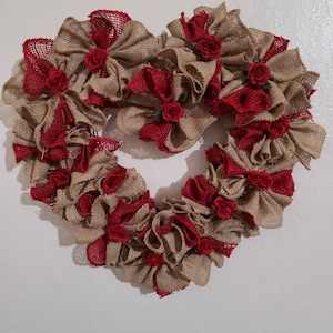 Puede incluir: Una corona en forma de corazón hecha de arpillera y tela roja con flores de tela roja.