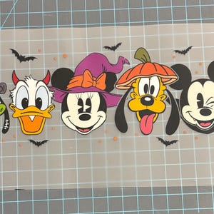 Könnte beinhalten: Ein Halloween-Motiv mit den Zeichentrickfiguren Goofy, Donald Duck, Minnie Mouse, Pluto und Mickey Mouse. Jede Figur ist in einem Halloween-Kostüm gekleidet, mit Fledermäusen und orangefarbenen Punkten.