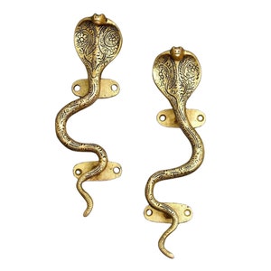Könnte beinhalten: Zwei messingfarbene Türgriffe in Kobraform. Die Griffe sind mit geätzten Mustern versehen und haben eine goldene Oberfläche. Jeder Griff hat einen Kobrakopf und einen geschwungenen Körper mit Montageplatten.
