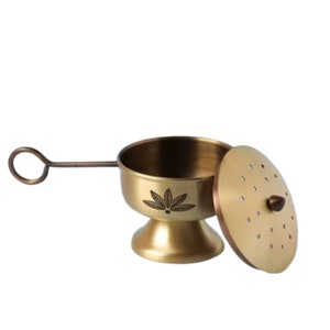 May include: A gold metal incense burner with a leaf design and a lid with holes. The burner has a handle.