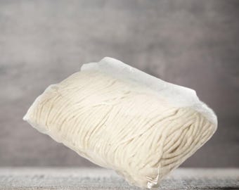 May include: A close-up of a white cotton yarn ball wrapped in clear plastic.