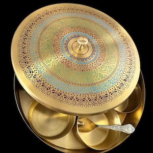 Op de afbeelding: Een goudkleurige kruidenbox met een decoratief deksel met een gedetailleerd, kleurrijk mandala-ontwerp. De doos heeft verschillende kleine compartimenten en een kleine lepel. Het deksel heeft een transparante knopgreep. De achtergrond is zwart.