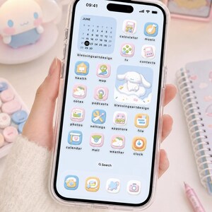 May include: A smartphone with a clear case displaying a light blue and pastel-themed interface. The screen features custom app icons, a June calendar widget, and a central graphic of a white cartoon character on a cloud with the text blessingsartdesign.