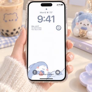 Op de afbeelding: Een doorzichtig smartphonehoesje op een mobiel apparaat met een digitaal vergrendelscherm met een witte achtergrond, een cartoonhaai onderaan, de tijd 9:41, de datum Mon 6 en de tekst Swipe up to unlock in het midden onderaan.