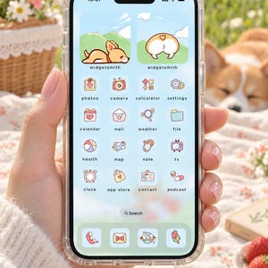 May include: A smartphone with a clear protective case displaying a custom light blue interface theme. The screen features two dog-themed widgets at the top and a grid of pastel-colored app icons labeled photos, camera, calculator, settings, calendar, mail, weather, file, health, map, note, tv, clock, app store, contact, and podcast.