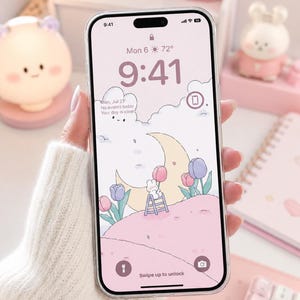 May include: A smartphone with a clear protective case displaying a digital wallpaper featuring a crescent moon, a small white rabbit on a ladder, and colourful tulips on a pink hill. The screen shows the time 9:41, date Mon 6, and weather 72 degrees.