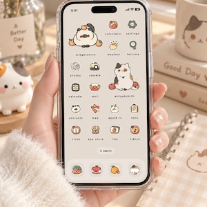 May include: A smartphone with a clear protective case displaying a custom home screen interface. The screen features a light cream background with various app icons and widgets illustrated with small cartoon cats, fruits, and soft-toned graphics.