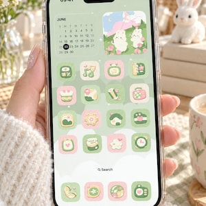 May include: A smartphone with a clear case displaying a custom light green and pink interface theme. The screen features a June calendar widget, a graphic of two white rabbits in a field, and a grid of pastel-colored app icons with various designs.