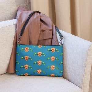 May include: A blue and orange patterned crossbody bag with a black strap. The bag has a zipper closure and a floral design.