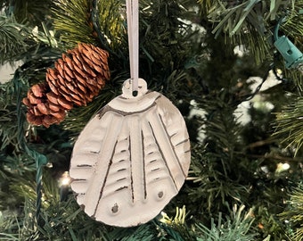 May include: White ceramic Christmas ornament with a geometric design. The ornament is hanging on a Christmas tree.