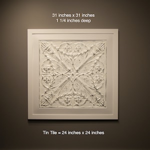 May include: A white framed wall art piece with a raised embossed design. The art piece is 31 inches by 31 inches and 1 1/4 inches deep. The text "Tin Tile = 24 inches x 24 inches" is below the art piece.