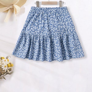 May include: A light blue skirt with a white floral print. The skirt has a ruffled hem and an elastic waistband.