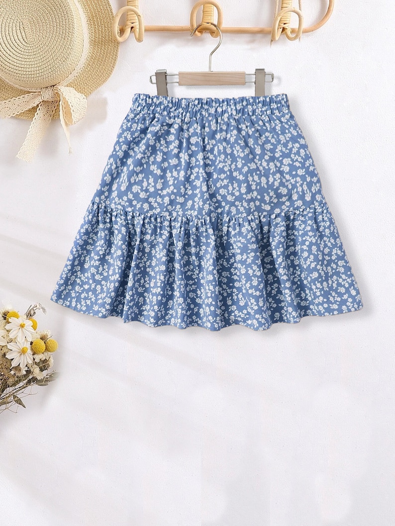 May include: A light blue skirt with a white floral print. The skirt has a ruffled hem and an elastic waistband.
