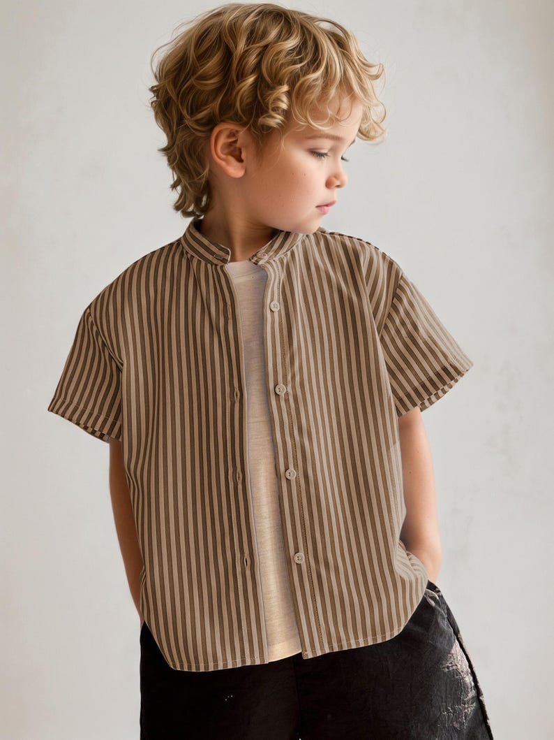 May include: A short-sleeved, button-down shirt with vertical brown and beige stripes. The shirt has a mandarin collar and is worn over a light-colored undershirt. The child is wearing black pants.