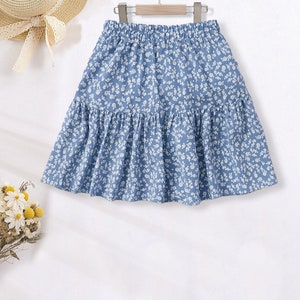 May include: A light blue skirt with a white floral pattern. The skirt has a gathered elastic waistband and a tiered design.