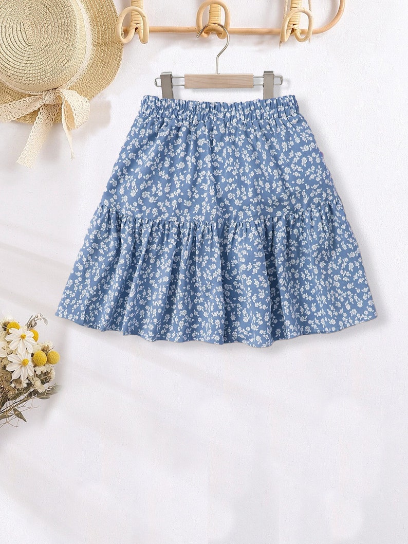 May include: A light blue skirt with a white floral pattern. The skirt has a gathered elastic waistband and a tiered design.