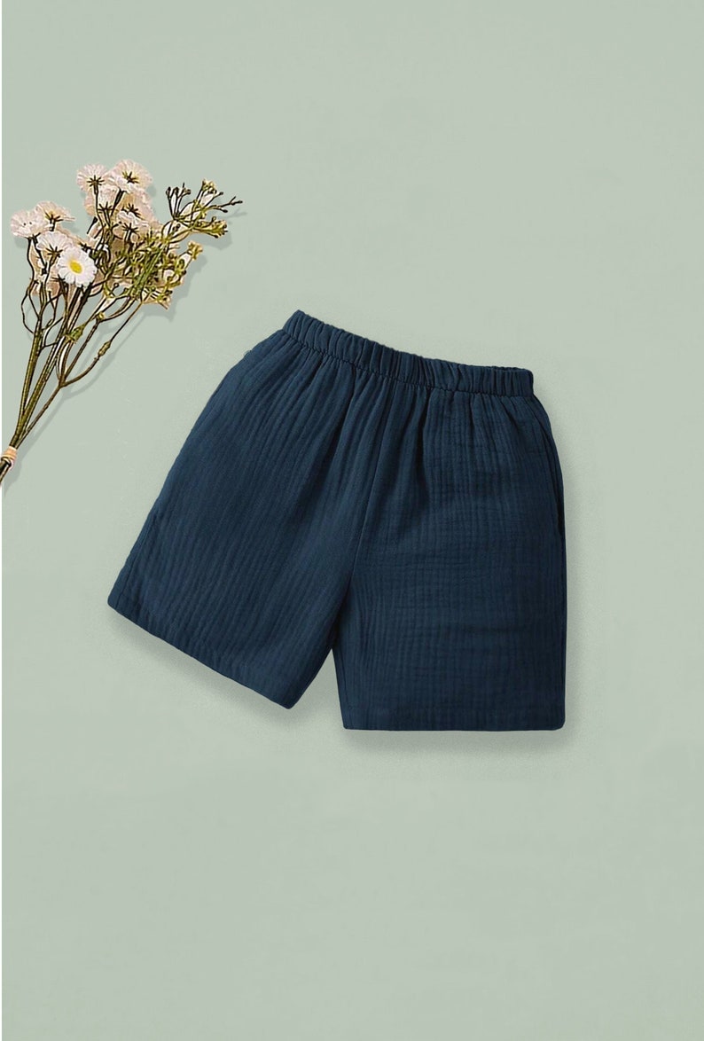 K&ouml;nnte beinhalten: Dunkelblaue Shorts mit elastischem Bund. Die Shorts sind aus einem strukturierten Stoff gefertigt und eignen sich f&uuml;r Freizeitkleidung. Ein Zweig mit wei&szlig;en Blumen befindet sich in der oberen linken Ecke des Bildes.