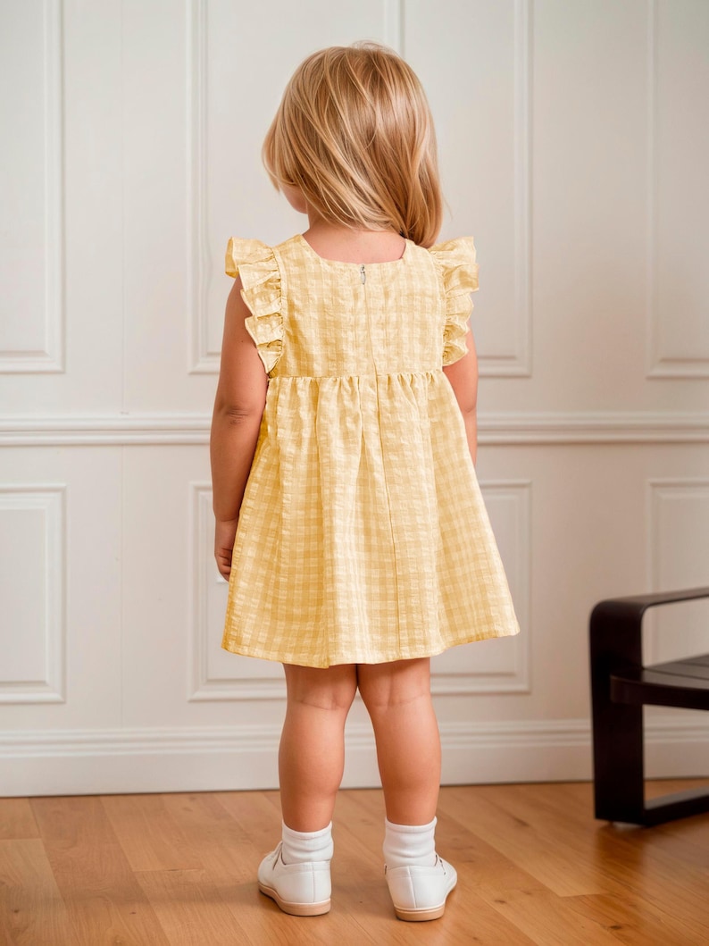 May include: A yellow plaid dress with ruffled sleeves. The dress is worn by a young child, who is facing away from the camera. The dress has a simple, classic design, perfect for a summer day. The child is wearing white socks and shoes.