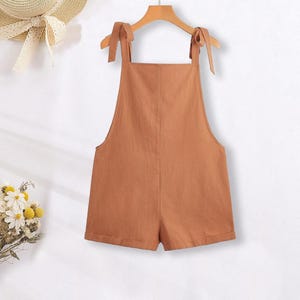 May include: A brown linen overall short with adjustable straps that tie at the shoulders.