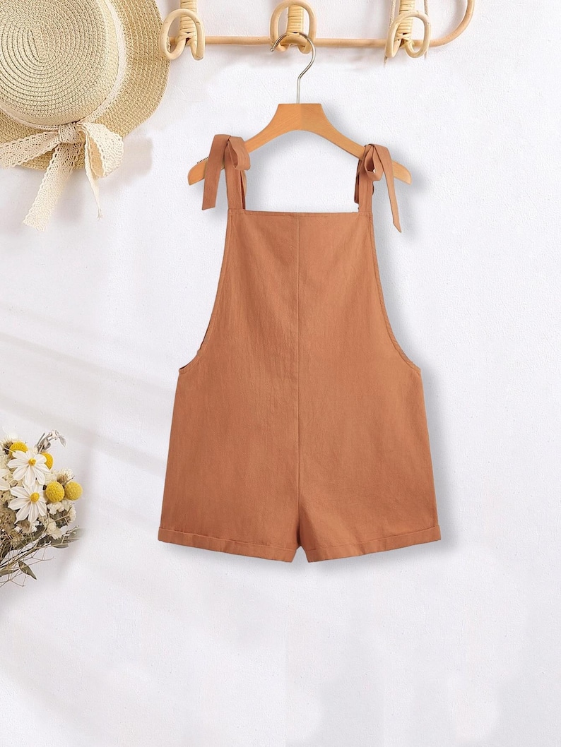 May include: A brown linen overall short with adjustable straps that tie at the shoulders.