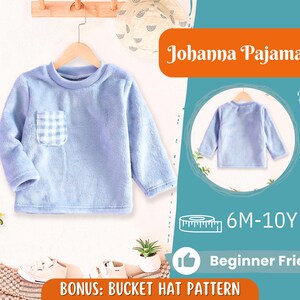 Pode incluir: Uma blusa de pijama azul claro com um pequeno bolso xadrez. A blusa de manga comprida é exibida em um cabide de madeira. O texto "Johanna Pajama" é visível. A imagem também inclui o texto "6M-10Y" e "Beginner Friendly".
