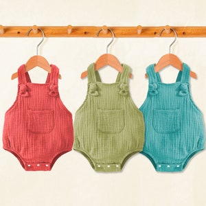 Puede incluir: Tres bodies de beb&eacute; colgados en un estante de madera. Los bodies est&aacute;n hechos de una tela suave y texturizada y tienen tirantes ajustables. Los bodies son de color rojo, verde y azul.