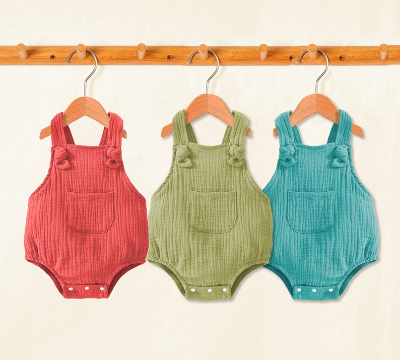 Puede incluir: Tres bodies de beb&eacute; colgados en un estante de madera. Los bodies est&aacute;n hechos de una tela suave y texturizada y tienen tirantes ajustables. Los bodies son de color rojo, verde y azul.