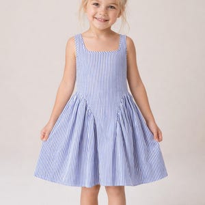 May include: A sleeveless blue and white striped dress with a square neckline. The dress has a pleated skirt and is worn by a young girl with blonde hair. The girl is smiling and standing barefoot.