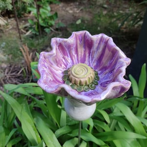Op de afbeelding: Een keramische bloem met een paarse en witte glazuur. De bloem heeft een groen centrum met een swirl-ontwerp en staat op een witte steel.