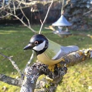Könnte beinhalten: Eine Keramik-Vogelfigur in Schwarz, Weiß, Grün und Grau bemalt. Der Vogel sitzt auf einem Ast.