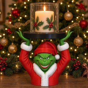 May include: A green character bust wearing a red and white Santa suit, holding a black circular platform above its head. A clear glass cylinder sits on the platform, containing a white pillar candle decorated with green pine sprigs and red berries.
