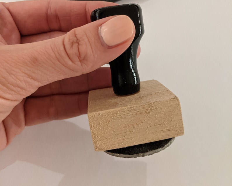 May include: A wooden stamp with a black handle. The stamp has a rectangular base and a round ink pad.