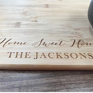 May include: A light brown wooden chopping board with the text "Home Sweet Home THE JACKSONS" engraved on the surface.