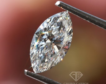 May include: A clear, marquise-shaped diamond held by tweezers against a blurred pink and green background. The diamond is sparkling and has a brilliant cut. The text "GROWN CARBON" is visible in the lower right corner of the image.