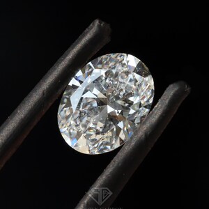 Może przedstawiać: Przezroczysty diament o owalnym kształcie trzymany przez pęsetę na czarnym tle.