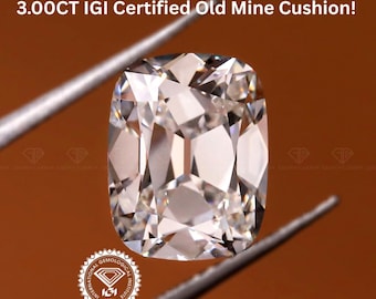 May include: A cushion-cut diamond, held by tweezers, against a brown background. The diamond is a light colour with many facets. Text at the top reads "3.00CT IGI Certified Old Mine Cushion!"