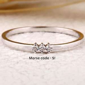 Könnte beinhalten: Ein silberner Ring mit drei kleinen, klaren Edelsteinen in einer Reihe. Der Ring ist dünn und zart, mit dem Text "Morse code - S!". Das Grown Carbon-Logo ist sichtbar. Der Ring ist etwa 0,2 cm breit.