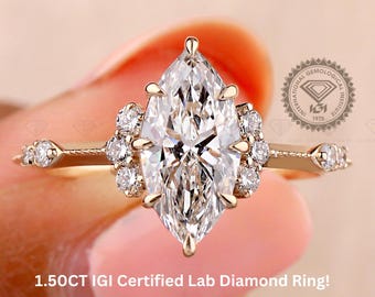 Könnte beinhalten: Ein goldener Ring mit einem Labor-Diamanten im Marquise-Schliff als Mittelstein. Der Ring hat kleinere Akzentsteine und zarte Details am Band. Der Text auf dem Bild lautet "1.50CT IGI Certified Lab Diamond Ring!"