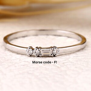 Könnte beinhalten: Ein zarter Silberring mit drei kleinen Diamanten. Der mittlere Diamant ist rechteckig, flankiert von zwei runden Diamanten. Der Ring ist vor einem weichen, neutralen Hintergrund platziert. Der Text "Morse code - F!" ist sichtbar.