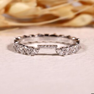 May include: A silver ring with a unique design. The ring features a series of small, round stones and larger, marquise-cut stones. The ring is designed to fit around another ring. The Grown Carbon logo is in the bottom right corner.