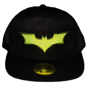 May include: Black mesh trucker hat with a yellow Batman logo on the front. The hat has a black brim and a black mesh back. The hat has a small tag on the front that says "Lowman Customs".