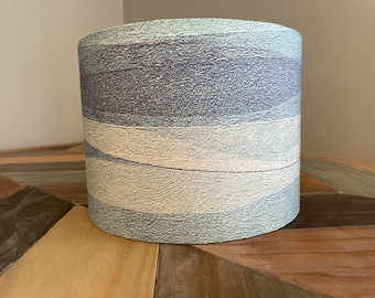 May include: A cylindrical lampshade with a blue, white, and gray abstract pattern. The pattern resembles waves or water.