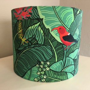 May include: A green and red lampshade with a tropical print featuring banana leaves and a red bird.