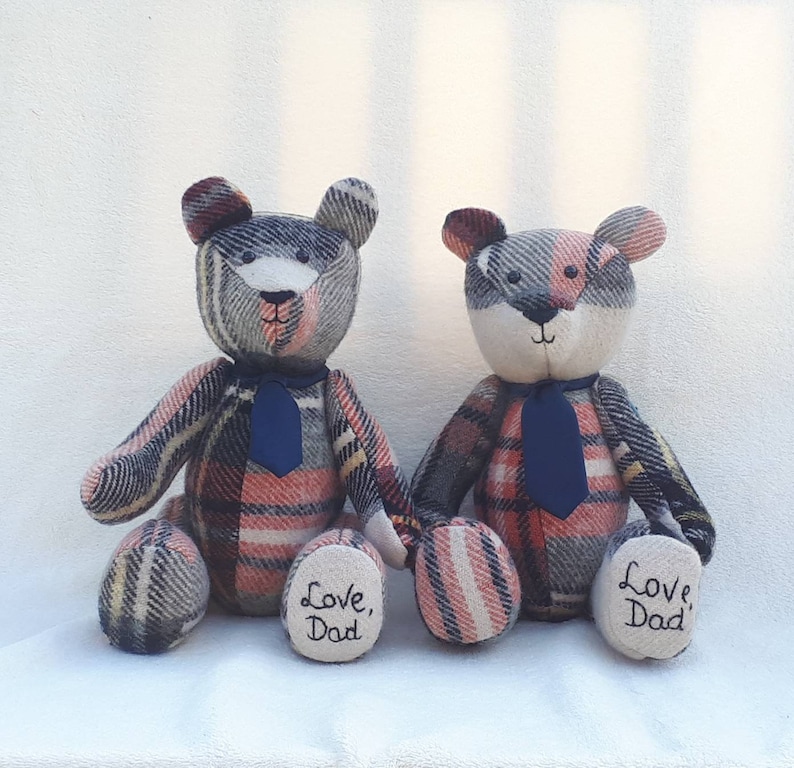 May include: Two plush teddy bears with a plaid pattern in shades of gray, pink, and blue. Each bear has a navy blue tie and the words "Love, Dad" embroidered on their paws.