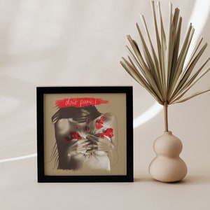 Könnte beinhalten: Ein gerahmter Druck mit einem schwarzen Rahmen und einem beigefarbenen Hintergrund. Der Druck zeigt eine Schwarzweißzeichnung einer Person mit roten Blumen auf der Brust. Der Text "don't panic!" ist in Rot über dem Bild geschrieben.