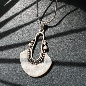 Könnte beinhalten: Eine silberne Halskette mit einem fächerförmigen Anhänger mit einem ausgeschnittenen ovalen Design und Perlenakzenten.